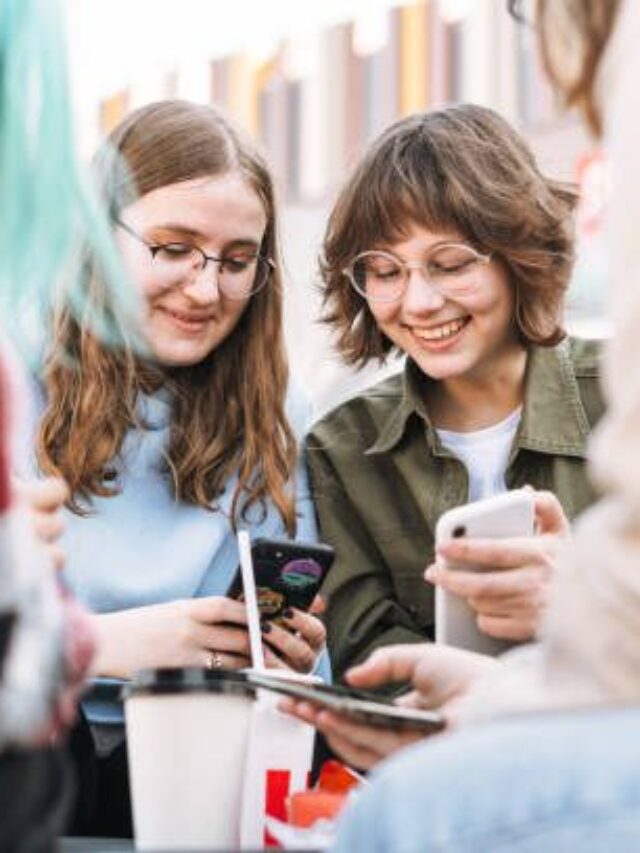 Group Of Teenage Girls Laughing Using Mobile Phone On Street At City